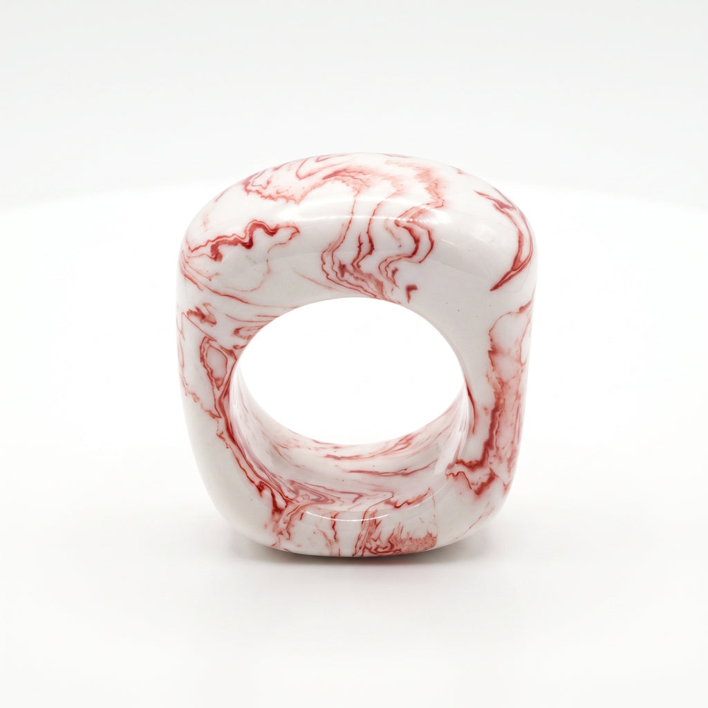 Petra Coral Small — anillo de porcelana blanca con vetas coral-rojo marmoladas a mano, forma cúbica redondeada, vista frontal sobre fondo blanco