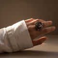 Camelia — anillo de porcelana con flor escultórica en acabado platino sobre aro fino plateado, vista frontal sobre fondo blanco mostrando el volumen y los pétalos modelados a mano