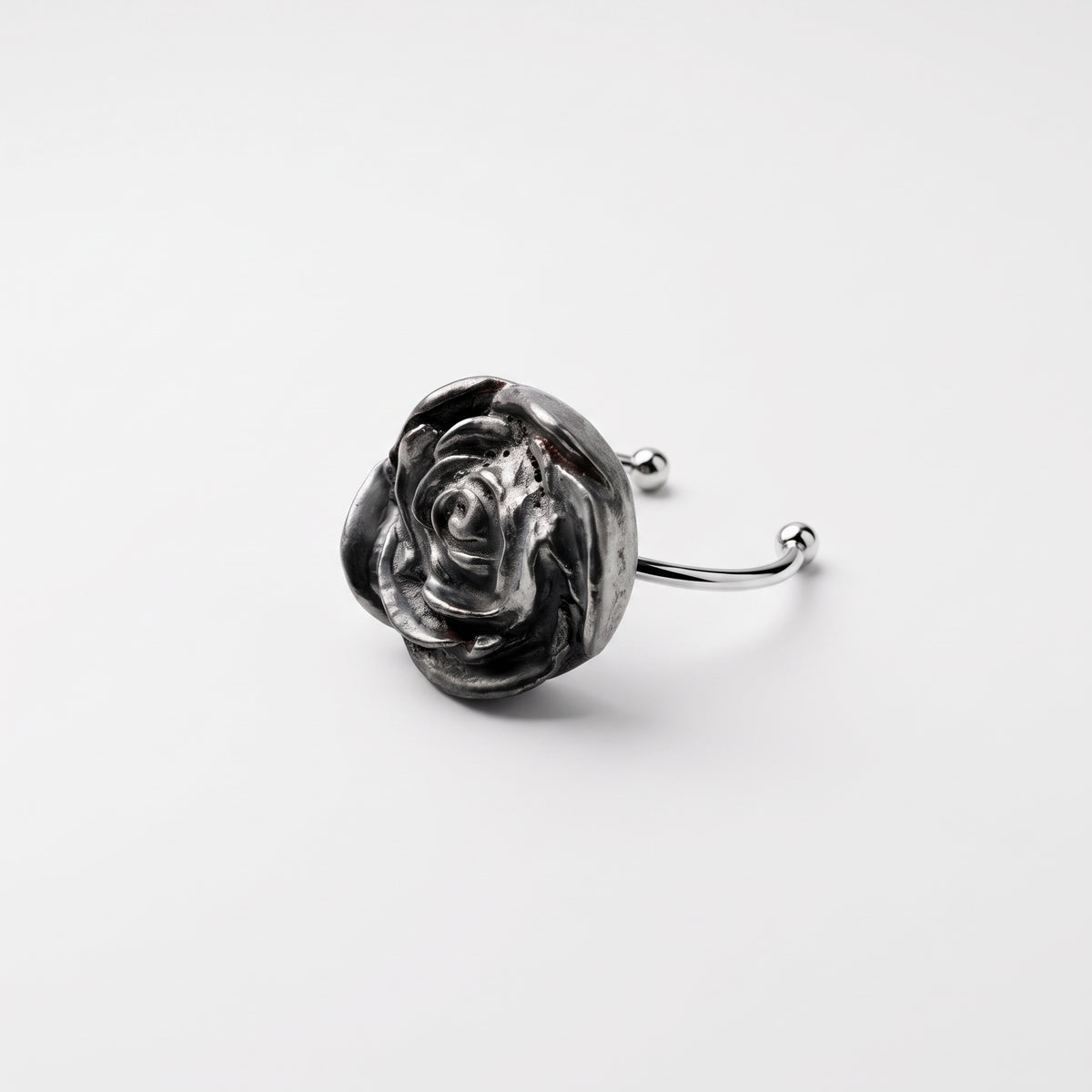 Camelia — anillo de porcelana platino en dedo índice, mano con camisa blanca sobre fondo beige cálido mostrando la escala y presencia de la flor