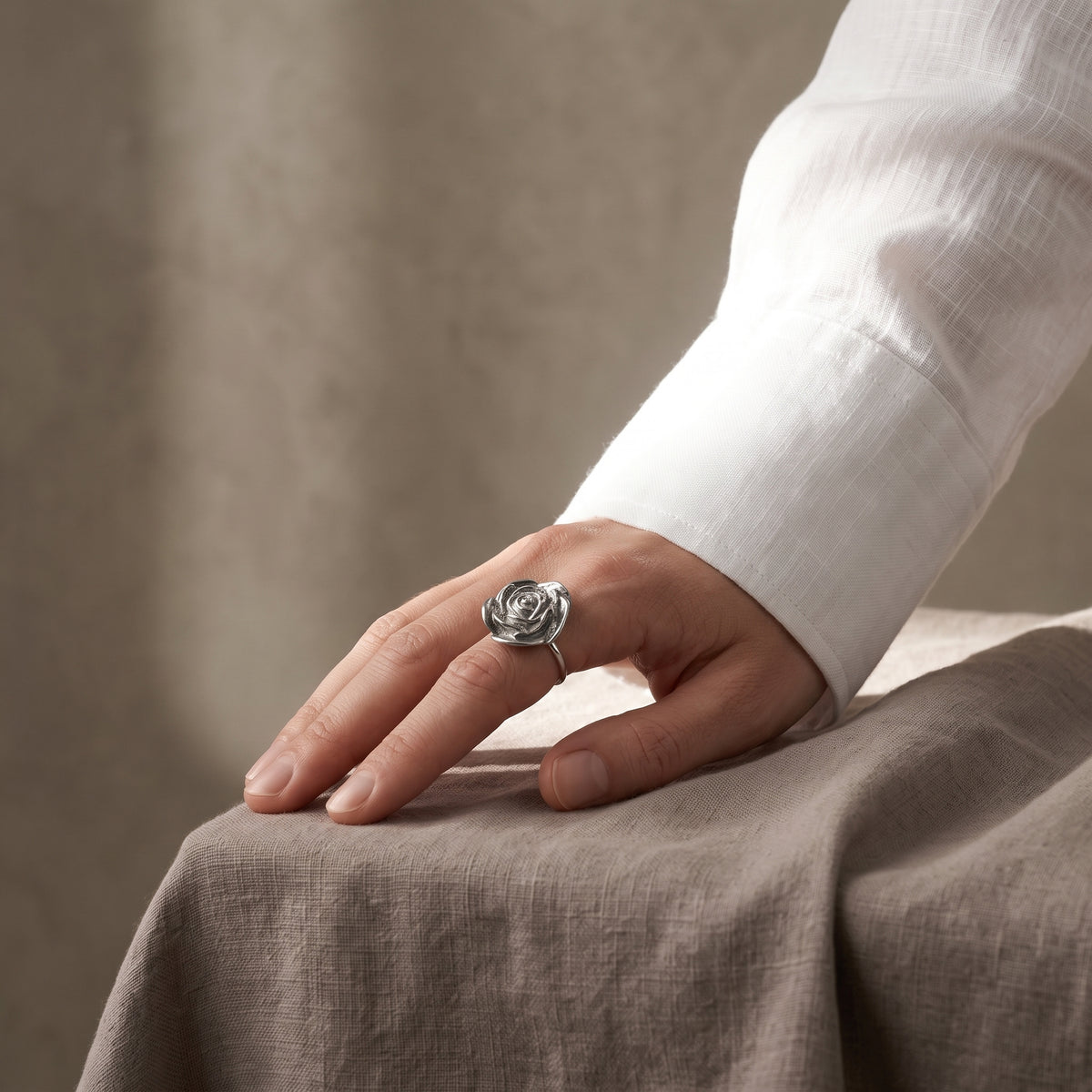 Camelia — anillo de porcelana platino en dedo corazón, manos entrelazadas con uñas burdeos oscuro sobre fondo beige cálido, vista editorial mostrando el contraste entre el platino y el acabado oscuro