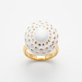 Girándola Blanco Oro S — anillo en dedo índice de mano femenina con camisa blanca, fondo beige cálido con luz lateral suave