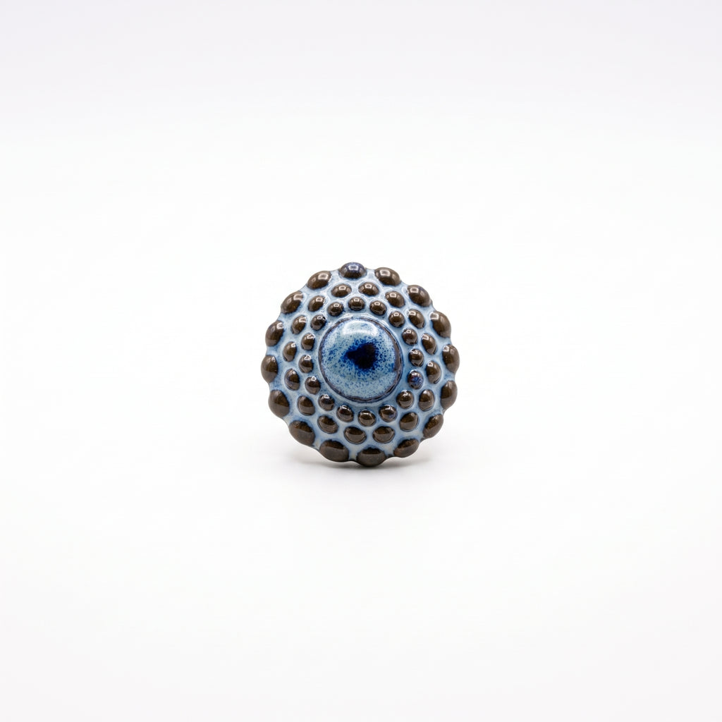 Girándola Azul Pizarra — anillo de porcelana con esfera de bultos en azul pizarra y puntos marrón oscuro sobre aro fino dorado con terminación en bola, vista lateral sobre fondo blanco