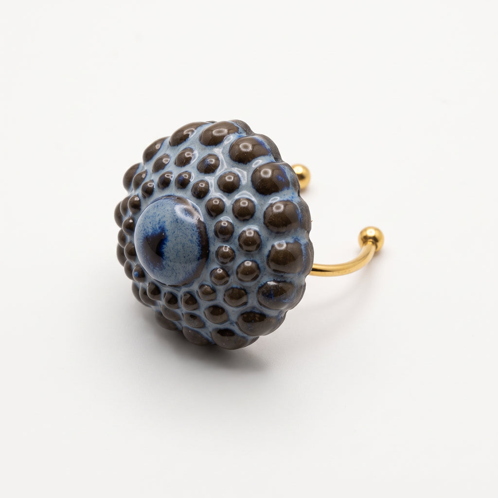 Girándola Azul Pizarra — modelo con camisa blanca y anillo en dedo índice, mano apoyada en el cuello, luz lateral cálida sobre fondo beige oscuro con flores secas