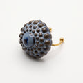 Girándola Azul Pizarra — modelo con camisa blanca y anillo en dedo índice, mano apoyada en el cuello, luz lateral cálida sobre fondo beige oscuro con flores secas