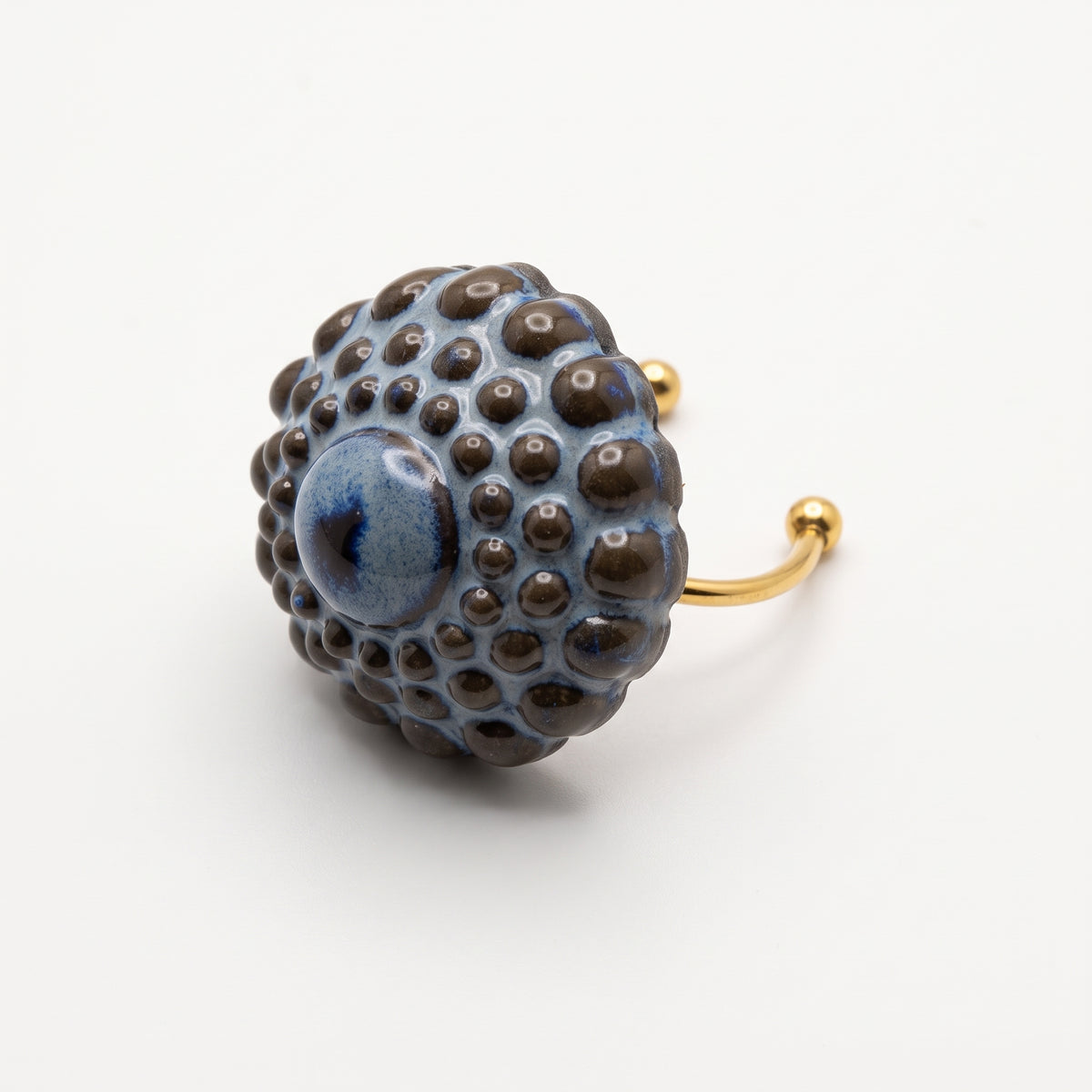 Girándola Azul Pizarra — modelo con camisa blanca y anillo en dedo índice, mano apoyada en el cuello, luz lateral cálida sobre fondo beige oscuro con flores secas