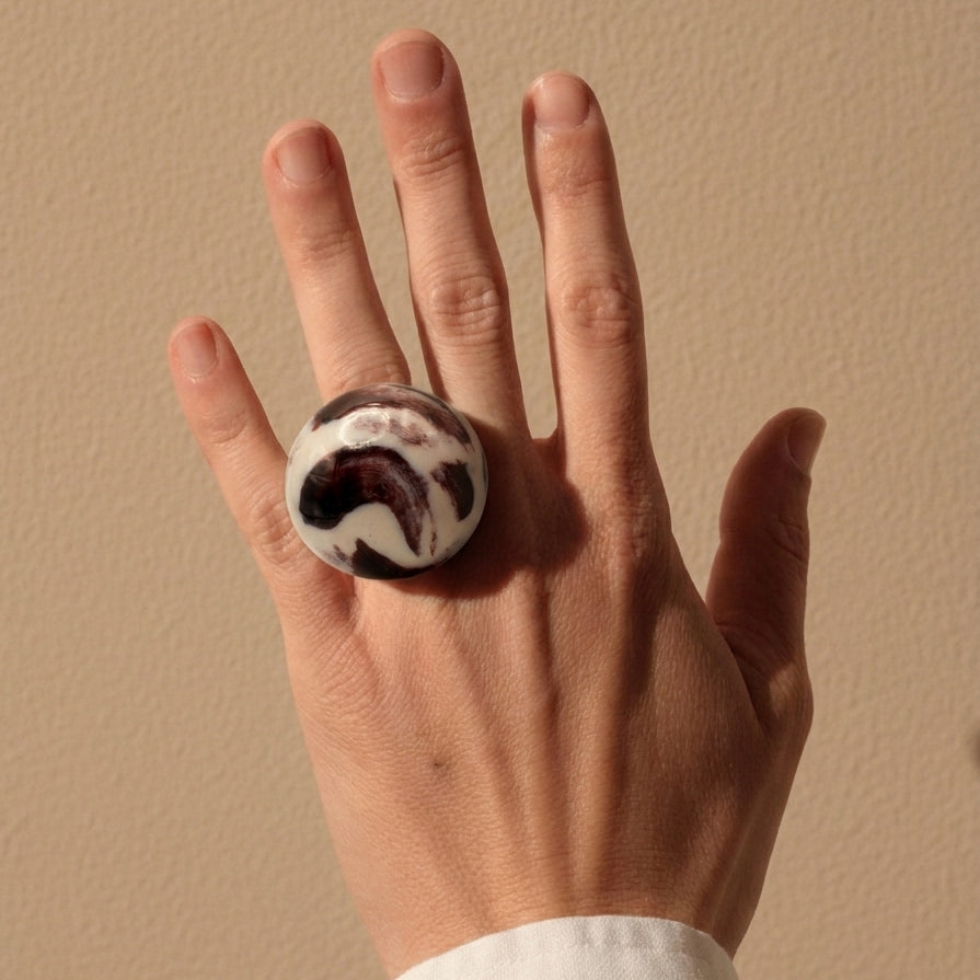 Trazo Lila — anillo de porcelana con cúpula esférica burdeos lila y aro ancho blanco mate, vista lateral sobre fondo blanco mostrando el volumen y la estructura